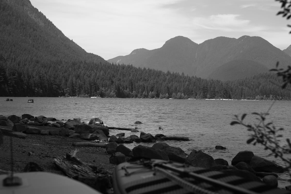A black and white photograph of a lake with some paddle boards in the frame